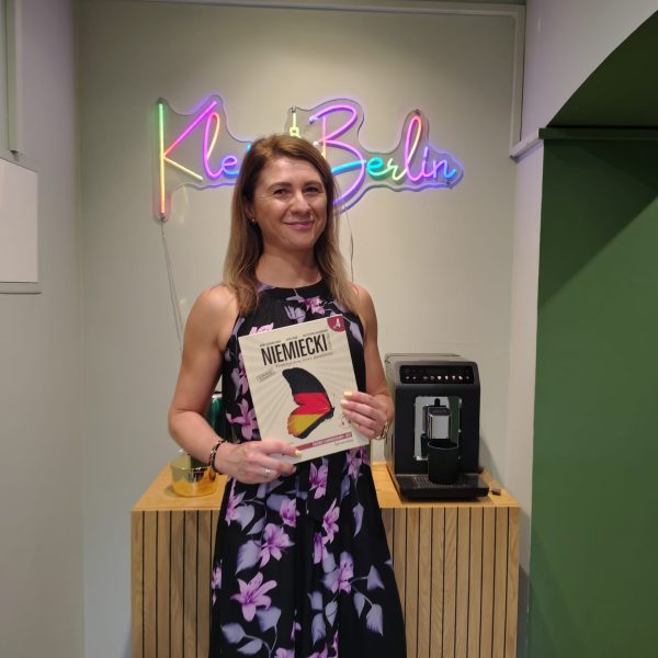 Dr Ewa Iglewska z podręcznikiem niemieckiego pod neonem Klein Berlin